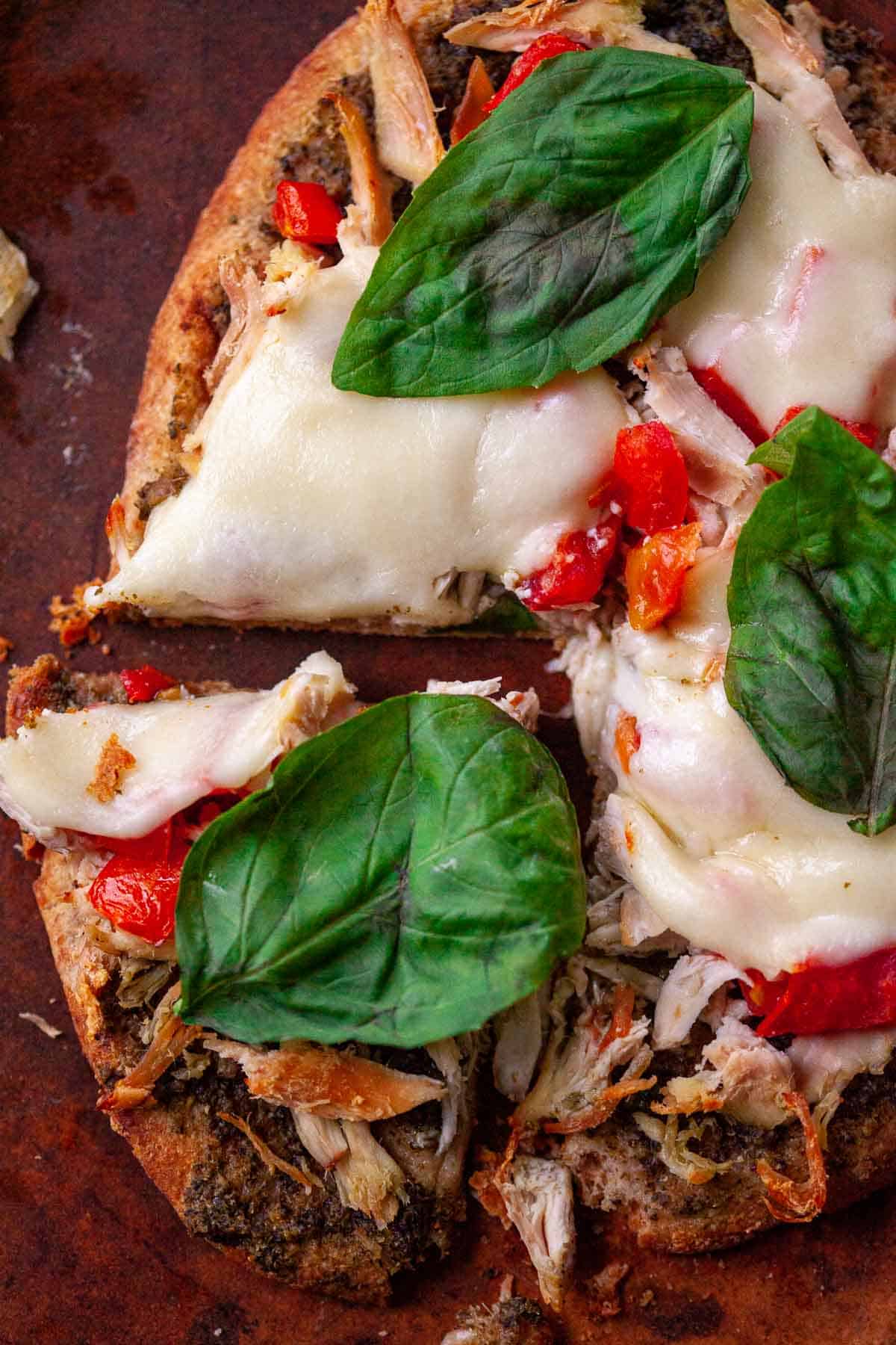 flatbread pizza with chicken, pesto, tomatoes, mozzarella cheese, basil with one slice cut