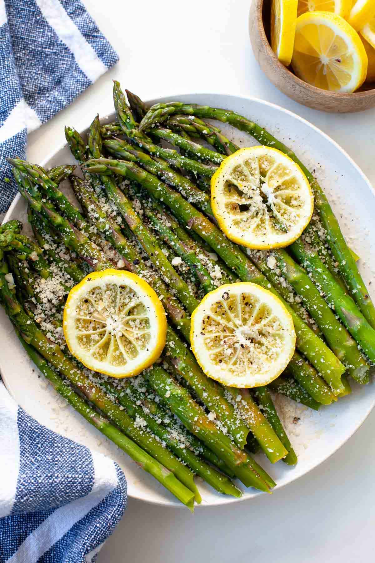 green asparagus in white bowl with lemons on white background, blue striped napkin