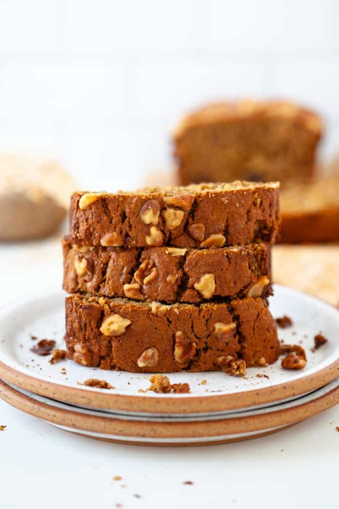 three stacked oat flour banana bread slices on white plate with banana bread slice in background