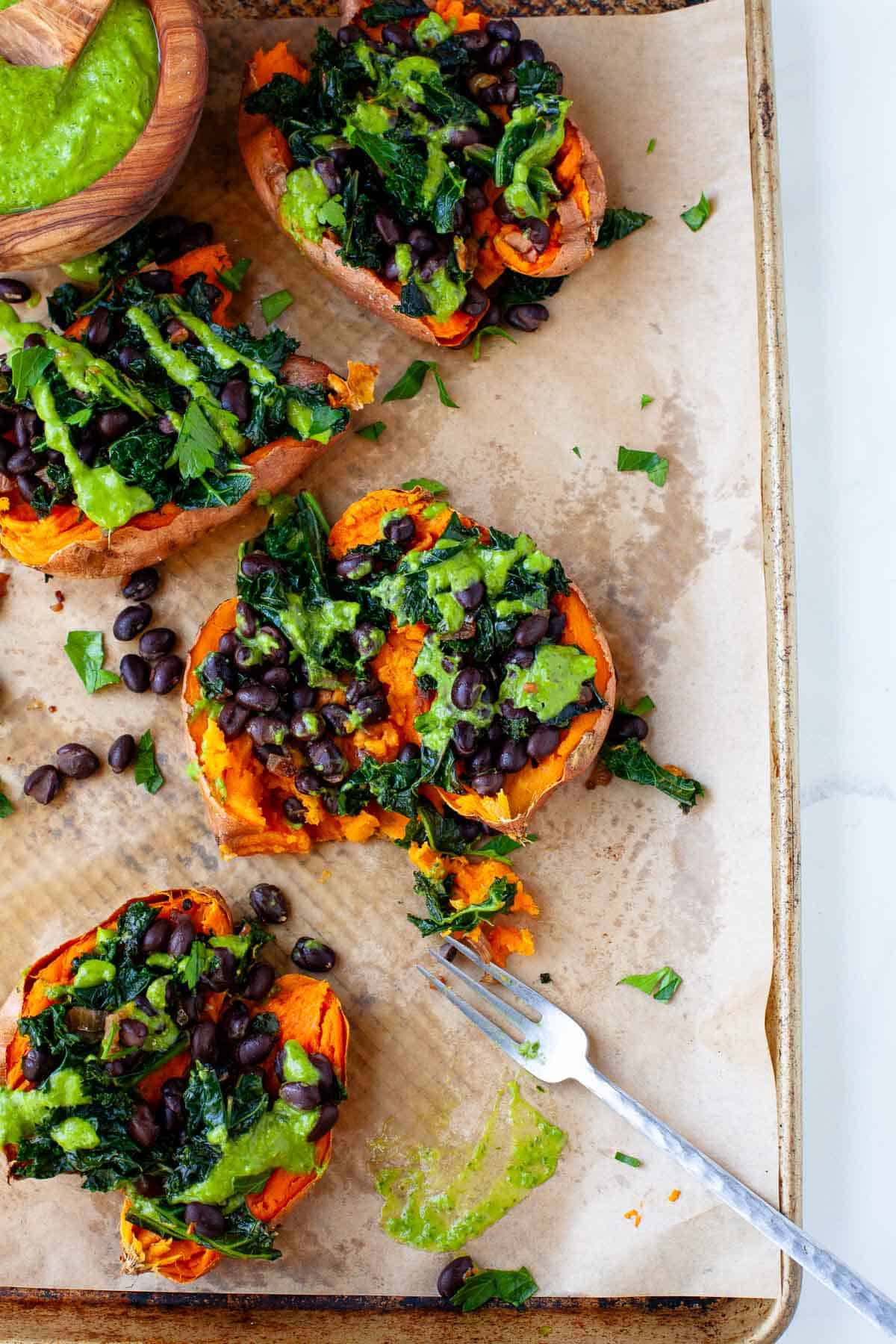 vegan loaded sweet potatoes with green goddess dressing on baking sheet lined with parchment paper.