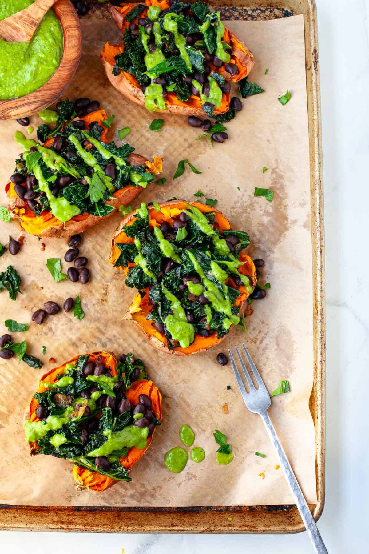 vegan loaded sweet potatoes topped with green goddess dressing and garnished with chopped fresh parsley on a baking sheet lined with parchment paper